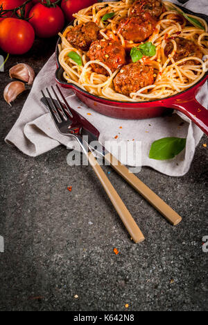 Spaghetti Nudeln mit Hackfleischbällchen, Tomatensauce Basilikum in Rot gusseisernen Pfanne, auf schwarzen Stein Tabelle kopieren Raum Stockfoto