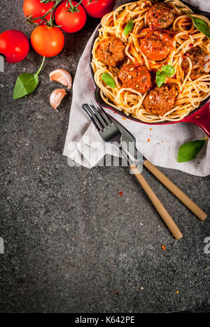 Spaghetti Nudeln mit Hackfleischbällchen, Tomatensauce Basilikum in Rot gusseisernen Pfanne, auf schwarzen Stein Tabelle kopieren Raum, Ansicht von oben Stockfoto