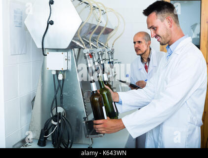 Lächelnder Mann, der weiße Mantel mit Abfüllanlagen für Wein die Manufaktur Stockfoto