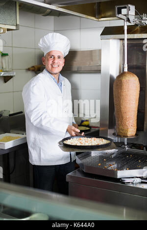 Reifer Mann Chef tragen einheitliche Vorbereitung Pizza in der Pfanne auf Küche im Cafe Stockfoto
