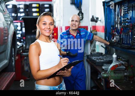 Junge lächelnde Frau, und schreiben Sie die Daten in dem Auto Service Stockfoto