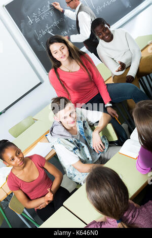 Freundliche junge Studenten verschiedener Nationalitäten sitzen und Lächeln im Klassenzimmer während der Pause Stockfoto