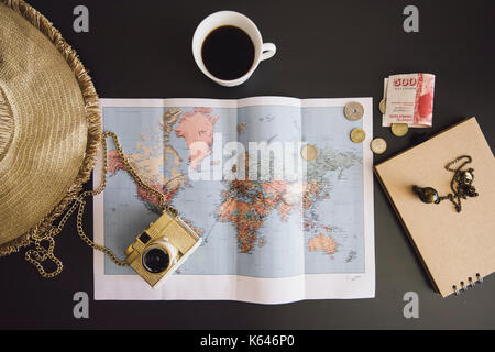 Die Planung der Reise. Weltkarte mit den Hut, Kamera, etwas Geld, Notebook aus Recyclingpapier und frisch gebrühten Kaffee Tasse auf der dunklen Tabelle Stockfoto