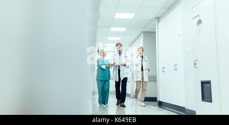 Gruppe der Mediziner mit Zwischenablage Krankenhaus Flur entlang zu laufen. Arzt und Krankenschwester diskutieren Ärztlicher Bericht mit weiblichen Kollegen sprechen über mobile Pho Stockfoto