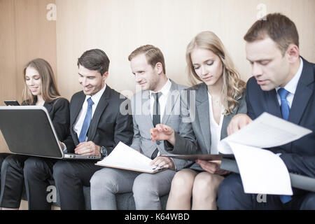 Geschäft Leute zusammen sitzen in einer Reihe in Lobby und Holding Laptop und Dokumente auf Knie Stockfoto