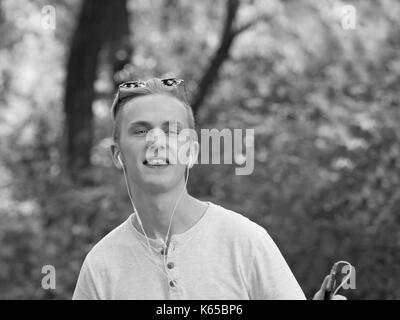 Kaukasischen jungen Mann in Blau runde Sonnenbrille mit Kopfhörern und Smartphone in seiner Hand Tanz Stockfoto