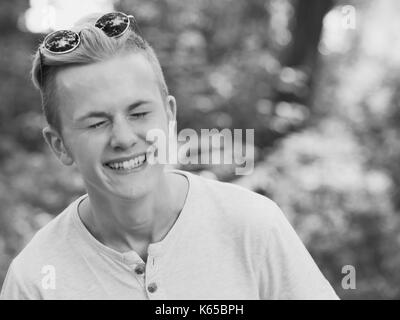 Kaukasischen jungen Mann mit blauen runde Sonnenbrille auf der Stirn lächelnd Stockfoto