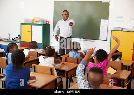 Lehrer und Kinder mit hands up in einer Grundschule Klasse Stockfoto