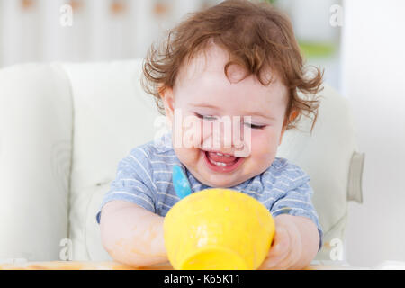 Cute baby boy Essen selbst auf hoher Stuhl Stockfoto