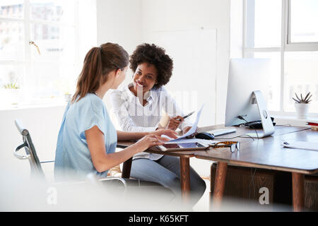 Zwei junge Frauen diskutieren Dokumente an einem Schreibtisch in einem Büro Stockfoto