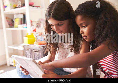 Zwei Mädchen sitzen auf dem Bett mit digitalen Tablet zusammen Stockfoto