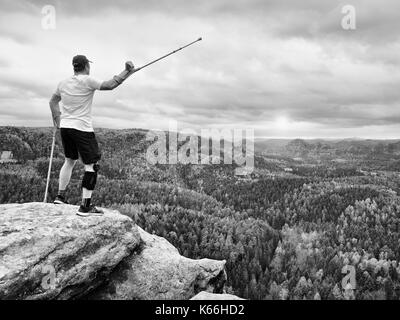 Glückliche Menschen Wanderer holding Medizin Krücke über dem Kopf, verletzte Knie Knie fest programmierte Strebe. Scenic mountain top mit tiefen nebligen Tal unten Stockfoto