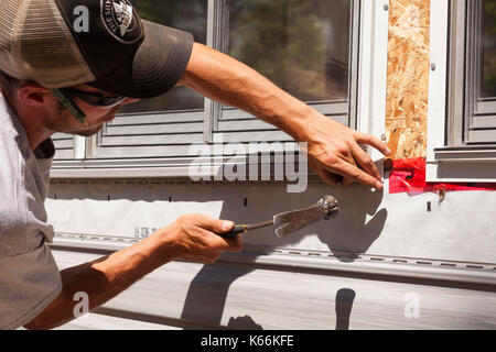 Ein Bauarbeiter hämmerten einen Nagel zu sichern Vinyl um ein Fenster in Ontario, Kanada. Stockfoto