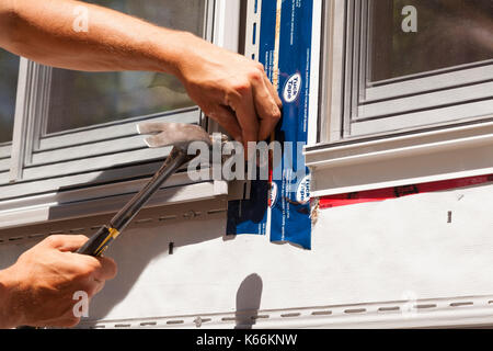 Ein Bauarbeiter hämmerten einen Nagel zu sichern Vinyl um ein Fenster in Ontario, Kanada. Stockfoto