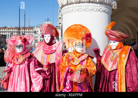 2017 Karneval in Venedig, Italien. Vier hell orange und magenta Kostüme in Piazza San Marcoposing vor einer Säule auf der Dogenpalast auf einem sonnigen Stockfoto