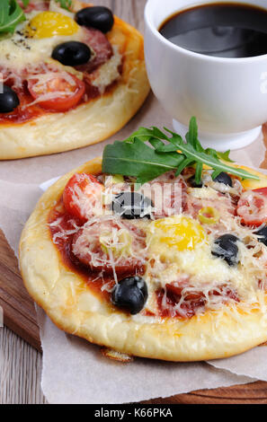 Mini-Pizza mit Rucola, eine Tasse Kaffee, Wurst und Ei Stockfoto