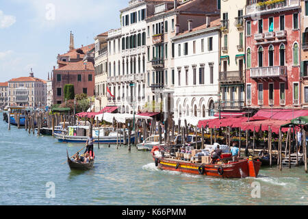 Bunte rote Boot transportieren große Flaschen Wein, Grand Canal, Venice, Italien im frühen Morgen Licht mit einem gondoliere Rudern eine Familie von Touristen Ich Stockfoto