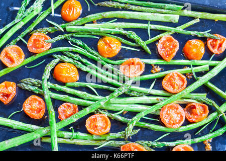 Gebratene frische Grüne Spargelspitzen und Cherry Tomaten gewürzt mit Rosmarin und Salz auf ein Backblech von oben gesehen für ein gourmet Vorspeise Stockfoto