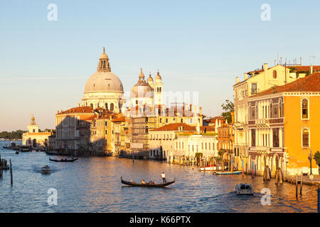 Sonnenuntergang auf den Canale Grande und die Basilika Santa Maria della Salute, Venedig, Italien mit einer Gondel und Boote auf dem Kanal. Warme goldene Stunde Licht. Stockfoto