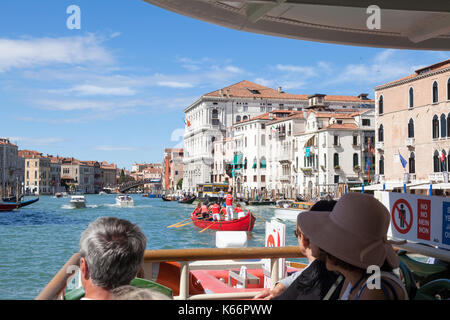 Touristen auf einem Vaporetto bis Reisen am Canal Grande, Venedig, Italien aus der ersten Person Sicht über den Bogen. Mannschaft der Venezianische Ruderer Stockfoto