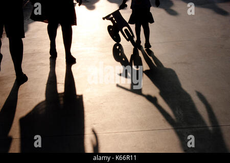 Verschwommene Schatten von einer Familie mit kleinen Mädchen treibt ein kleines Fahrrad auf Sommer promenade Stockfoto