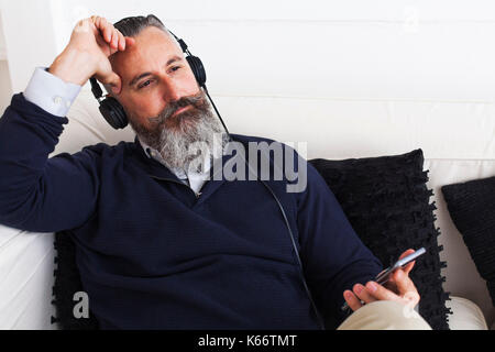 Nachdenklich kaukasischen Mann hören auf Handy mit Kopfhörer Stockfoto