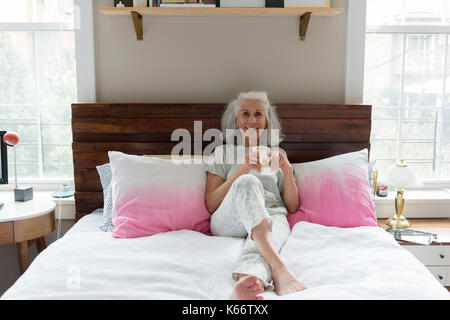 Lächelnde ältere Frau trinkt Kaffee im Bett Stockfoto