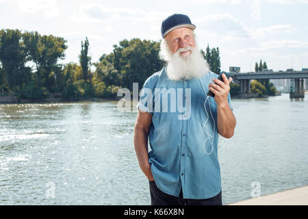 Bärtige stilvolle reifer Mann im Kopfhörer ist das Hören von Musik mit einem Smartphone Stockfoto