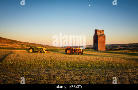 Traktoren und verlassenen Getreidesilo in der Geisterstadt Dorothy in Kanada bei Sonnenuntergang. Stockfoto