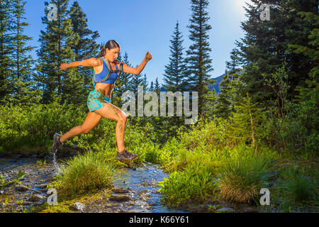 Hispanic Frau springen über Stream Stockfoto