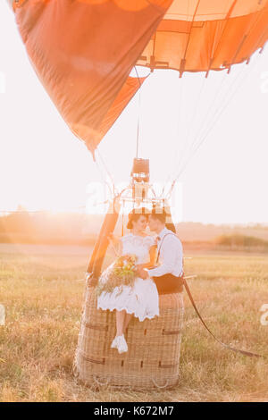 Die empfindlichen Augenkontakt betweet das glückliche Brautpaar sitzen auf dem airballoon Warenkorb in den sonnigen Tag im Feld. Stockfoto