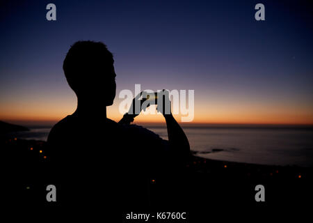 Man Fotos mit Telefon auf Strand, Silhouette bei Sonnenuntergang Stockfoto