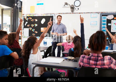 Schule Kinder heben die Hände in der Grundschule Klasse Stockfoto