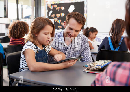 Lehrer und junge Schulmädchen mit Tablette im Klassenzimmer Stockfoto