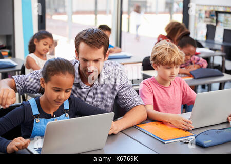 Lehrer helfen jungen Studenten mit Laptops in der Klasse Stockfoto