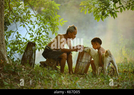 Großvater und Enkel im Wald Sitzen, Spielen mit einem Hund, Thailand Stockfoto