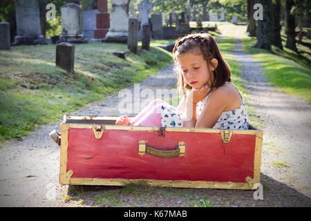 Kleines Kind in ein rotes Kästchen ist traurig auf einem Friedhof Stockfoto