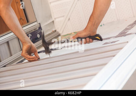 Ein Bauarbeiter hämmerten einen Nagel Vinylabstellgleis um ein Fenster in Ontario, Kanada zu sichern. Stockfoto