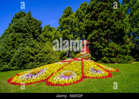 Eine bunte Statue eines Pfau wird durch Blumen Stockfoto
