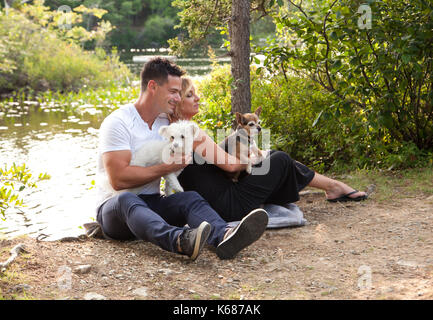 Eine schöne blonde Frau hält einen kleinen braunen Hund, und lehnt sich zurück entspannt gegen ihr schöner Mann an der lakea Stockfoto