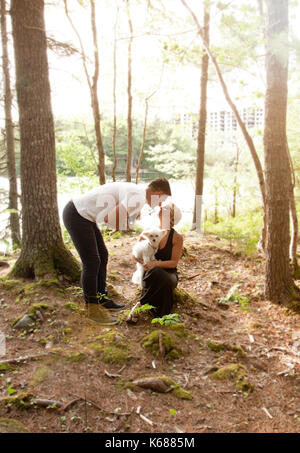 Ein weiches Sommer Glühen im Wald an einem See, wo ein Mann und eine Frau, die ihre Hunde und Kiss halten Stockfoto