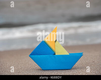 Blau und Gelb Papier Boot am Strand Sand gegen das Meer Stockfoto