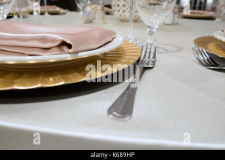 Eine Gabel neben eine goldene Platte auf einem weissen Satin Tischdecke sitzen. Stockfoto