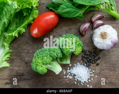 Grünes Gemüse und Gewürze, Salat, Spinat, lila Knoblauch, zwei Brokkoli Köpfe, eine rote Tomate, schwarzer Pfeffer und Salz, Holz- Hintergrund Stockfoto