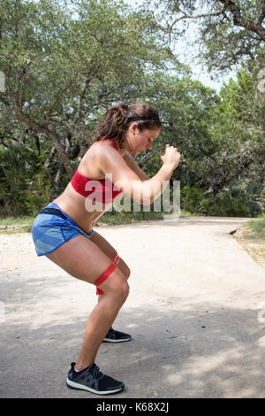 Junge Frau, die an Ihren Antrieb das Tragen der roten Sport-BH und Shorts hockt tun Stockfoto