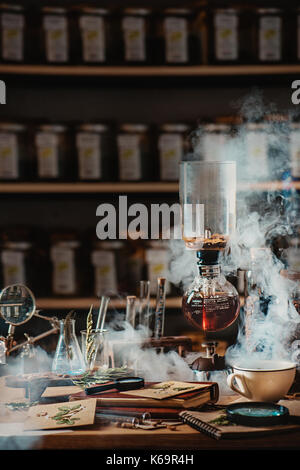 Die Zubereitung von Kaffee im Vakuum Kaffeemaschine mit aufsteigenden Dampf und einem Blumen still life. Alternative Kaffee brühen. Botaniker Arbeitsplatz. Professionelle b Stockfoto