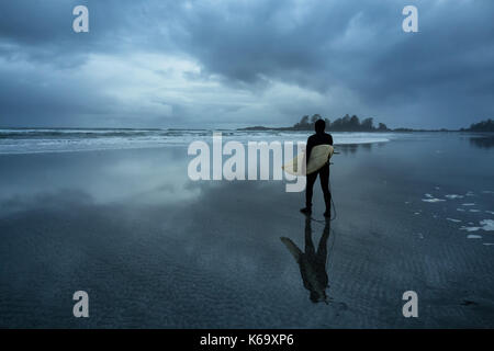 Surfer, die heraus im Ozean, während eine trübe winter Sonnenuntergang. Bild in Chesterman Beach, Tofino, Vancouver Island, BC, Kanada. Stockfoto