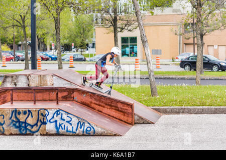 Saguenay, Kanada - Juni 3, 2017: Downtown City Sommer Park in Quebec mit junger Teenager boy Skaten, Tricks, Stunts auf Roller, Reiten auf Stockfoto