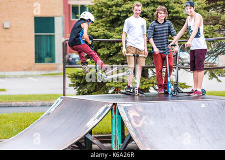 Saguenay, Kanada - Juni 3, 2017: Downtown City Sommer Park in Quebec mit jungen jugendlichen Jungen skaten, Durchführung tailwhip Tricks, Stunts auf Scooter Stockfoto