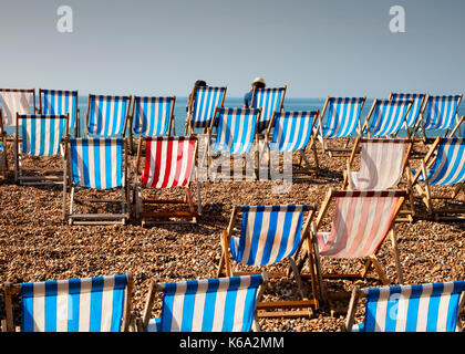 Zwei Personen sitzen auf Liegestühlen am Strand von Brighton Stockfoto